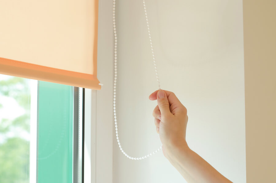 Damska dłoń trzymająca sznurek z koralikami do regulacji rolet